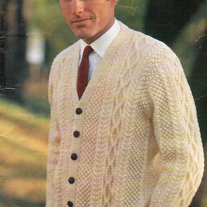May include: A cream-colored cable knit cardigan with a dark red tie and black buttons. The cardigan has a V-neck and long sleeves.