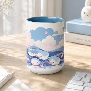Könnte beinhalten: Zylindrische Keramiktasse mit blauem Innenraum und weißem Äußeren. Sie zeigt ein skurriles Design von blauen und weißen Wasserlebewesen vor dem Hintergrund von Wolken und Blumen. Die Tasse steht auf einem Holztisch.