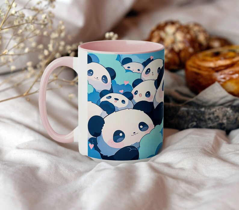 Op de afbeelding: Een witte keramische mok met een roze rand heeft een ontwerp met schattige cartoon-panda's met blauwe en witte accenten. De panda's zijn omringd door blauwe wolken en roze harten.