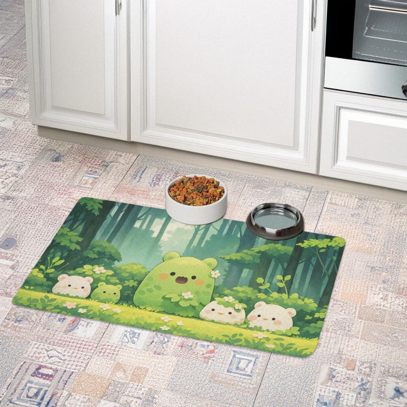 May include: A rectangular pet food mat featuring a whimsical forest scene with cartoon bears. The mat is green with a forest background and has a white and a silver pet bowl on top. A white ceramic bowl filled with pet food is also on the mat.