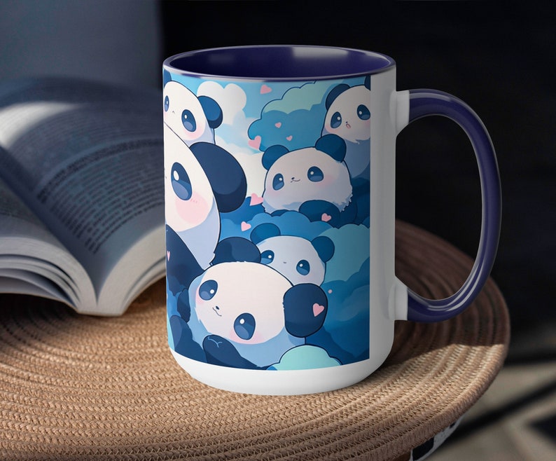 Op de afbeelding: Een witte keramische mok met een blauwe rand en handvat. De mok heeft een ontwerp met meerdere cartoonpanda's met blauwe en witte wolken en harten. De panda's lachen allemaal en hebben zwarte ogen.