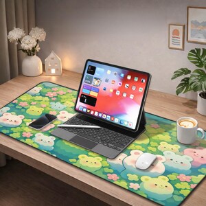 May include: A desk setup featuring a tablet with a keyboard, a smartphone, and a mouse on a colorful mousepad. The mousepad has a repeating pattern of cartoon bears and flowers. A white mug with a drink is on the right.