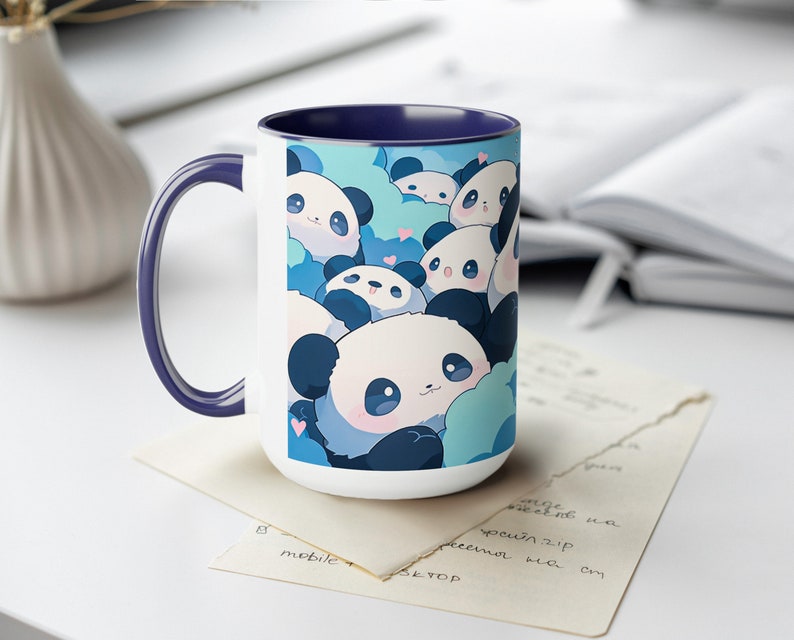 Op de afbeelding: Witte keramische mok met een blauwe rand en een ontwerp van schattige cartoon-panda's op een blauwe en witte achtergrond.