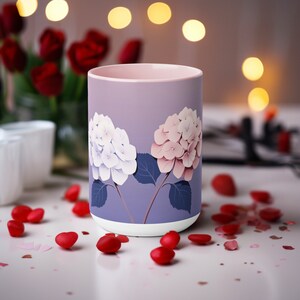 以下が含まれることがあります： ピンクと白の紫陽花が描かれた、紫色のセラミック製のマグカップ。テーブルの上に置かれており、周りに赤いハートが散らばっています。