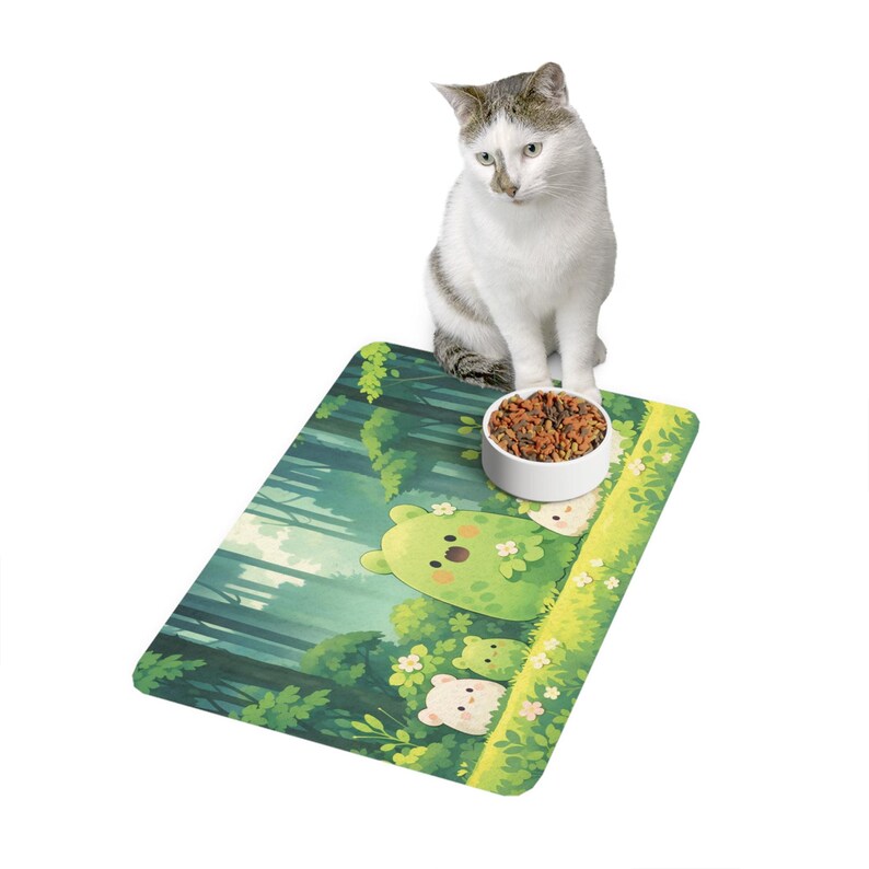 May include: A white cat sits near a food bowl on a green mat with a forest scene and cartoon bears. The mat has a rectangular shape and is decorated with green trees, grass, and white flowers. The bowl is white and filled with dry cat food.