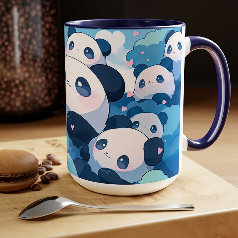 Op de afbeelding: Een witte keramische mok met een blauwe rand en handvat. De mok heeft een kleurrijke illustratie van meerdere cartoon-panda's met roze harten op een blauwe achtergrond.