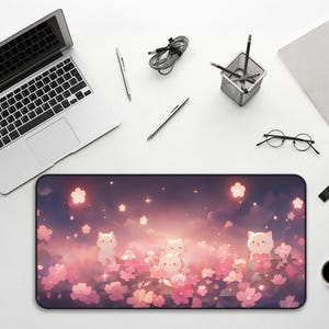 May include: A rectangular desk mat featuring a whimsical design with cartoon cats amidst pink flowers and a dreamy sky. The mat is surrounded by a laptop, pens, a pencil holder, a notebook, glasses, a smartwatch, and a coffee cup.