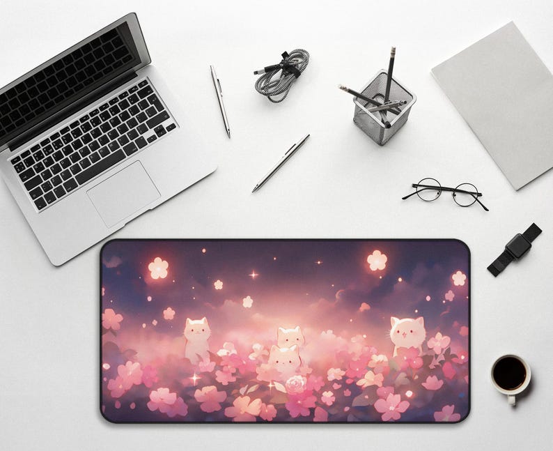 May include: A rectangular desk mat featuring a whimsical design with cartoon cats amidst pink flowers and a dreamy sky. The mat is surrounded by a laptop, pens, a pencil holder, a notebook, glasses, a smartwatch, and a coffee cup.