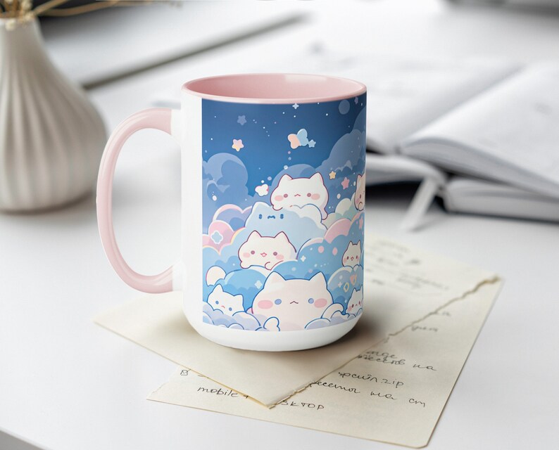 以下が含まれることがあります： ピンクの縁取りと持ち手のある白いセラミック製のマグカップ。マグカップには、青い空に雲と星が描かれた、カラフルな漫画の猫のイラストが描かれています。