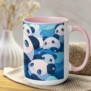Op de afbeelding: Een witte keramische mok met een roze rand en handvat. De mok heeft een kleurrijk ontwerp met cartoonpanda's met harten op een blauwe achtergrond.