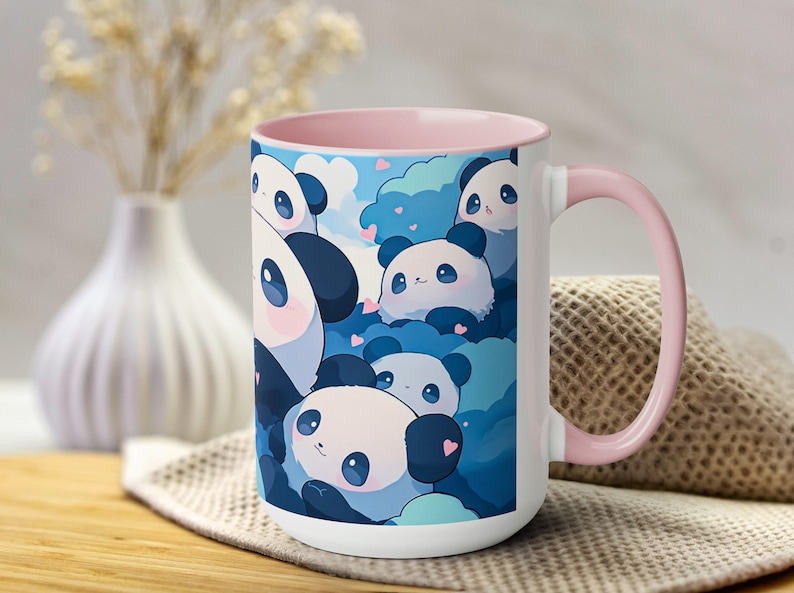 Op de afbeelding: Een witte keramische mok met een roze rand en handvat. De mok heeft een kleurrijk ontwerp met cartoonpanda's met harten op een blauwe achtergrond.