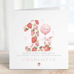 May include: A pink and white birthday card with a strawberry-patterned number one, a pink balloon that says "One", and a bunny holding a strawberry. The card says "Happy First Birthday to a Berry Special Granddaughter Charlotte".