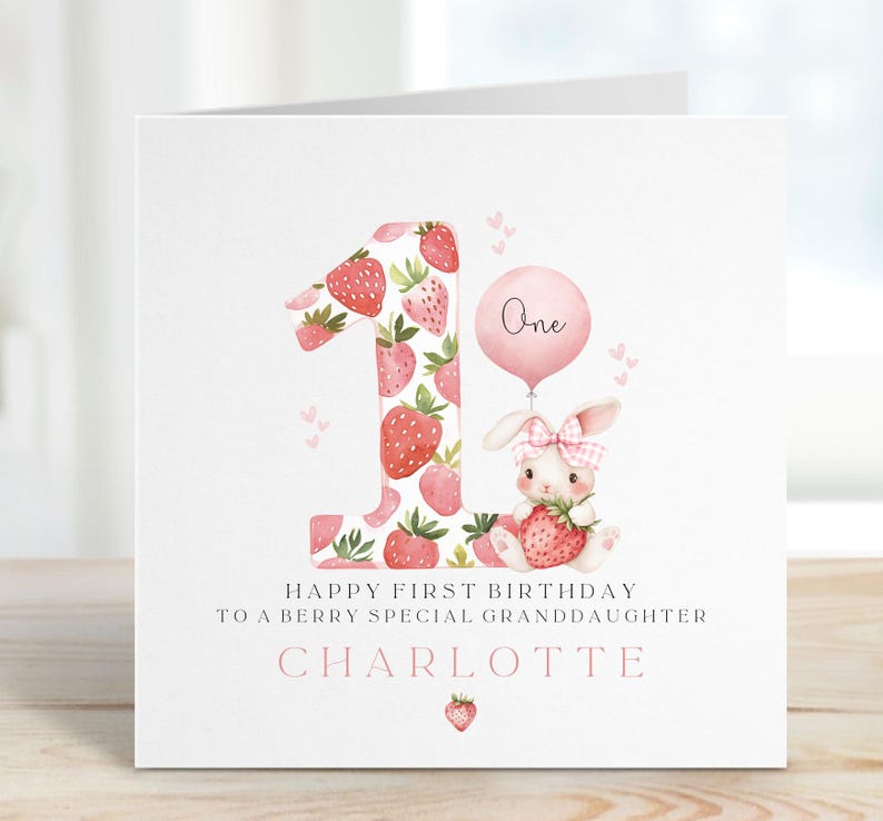 May include: A pink and white birthday card with a strawberry-patterned number one, a pink balloon that says "One", and a bunny holding a strawberry. The card says "Happy First Birthday to a Berry Special Granddaughter Charlotte".