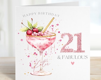 Op de afbeelding: Verjaardagskaart met een aquarel illustratie van een roze cocktail met kersen en een gouden rietje. De tekst "Happy Birthday" is aanwezig, met een glitterende "21" en "& FABULOUS". Een klein roze hartje staat onderaan.