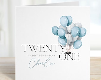 Puede incluir: Una tarjeta blanca con globos azules y blancos y el texto "TWENTY ONE" con una pajarita negra. El texto "HAPPY BIRTHDAY" y el nombre "Charlie" también están en la tarjeta.