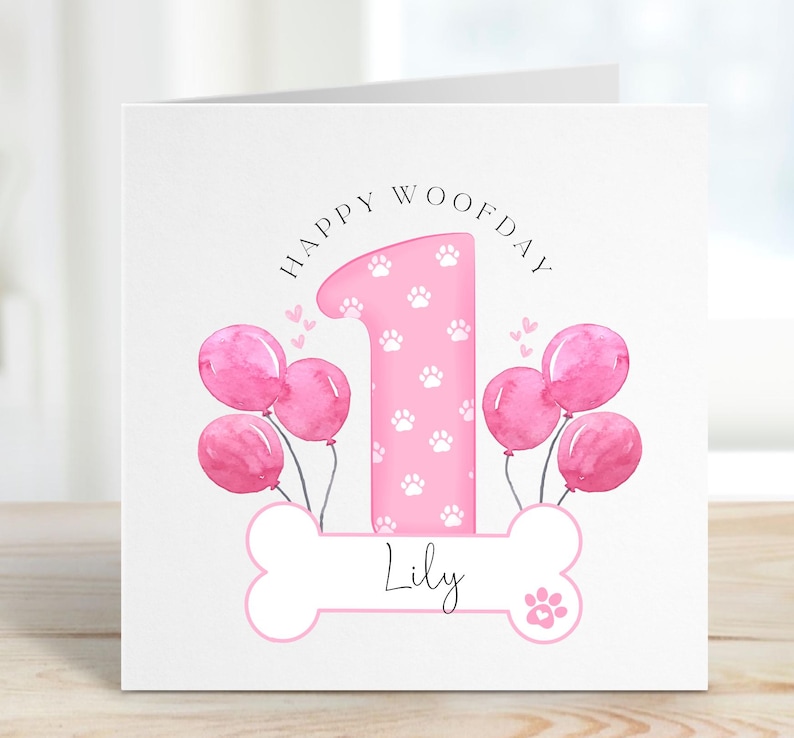 May include: Pink birthday card with a paw print design. The card says "Happy Woofday" and features a pink number one with paw prints. The card is personalised with the name "Lily".