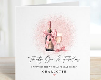 Puede incluir: Una tarjeta de cumpleaños rosa y blanca con una botella de champán y una copa de champán. La tarjeta dice "Twenty One & Fabulous" y "Feliz cumpleaños a una hermana especial Charlotte".