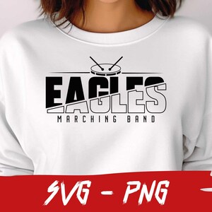 Pu&ograve; includere: Felpa bianca con un design grafico nero di un tamburo e il testo "EAGLES MARCHING BAND".