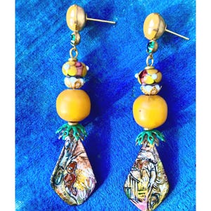 May include: A pair of long, dangling earrings with a yellow, green, and white glass bead design. The earrings feature a teardrop-shaped pendant with a colorful, abstract pattern.