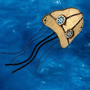May include: A wooden jellyfish mobile with black string tentacles and gears on the body. The mobile is hanging against a blue background.
