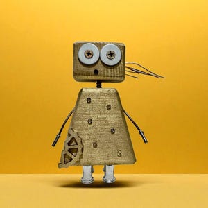 May include: A whimsical robot sculpture with a wooden head and body, featuring large, round eyes and metal accents. The robot has a gold-colored dress and wire arms, standing against a yellow background. The robot's height is approximately 6 inches.
