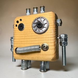 May include: A handcrafted wooden robot sculpture with a light brown body. The robot features metal hardware, including bolts, screws, and a gear-shaped embellishment. The robot has a spring for a mouth and metal legs.
