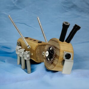 May include: A wooden toy ant with metal legs and antennae. The ant has a gear on its back and is painted brown.