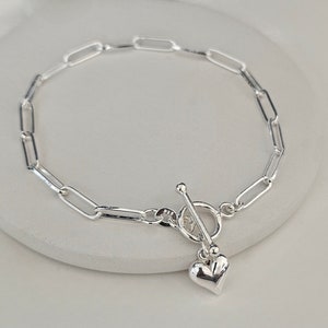 Puede incluir: Un brazalete de cadena de plata con un dije de coraz&oacute;n y un cierre de palanca.
