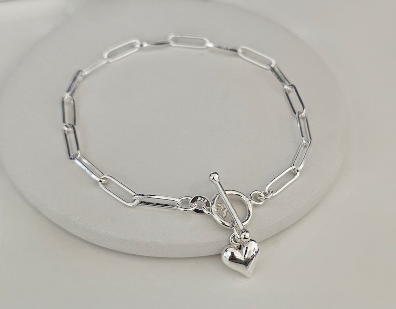 Puede incluir: Un brazalete de cadena de plata con un dije de coraz&oacute;n y un cierre de palanca.