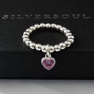 Könnte beinhalten: Ein silberner Ring mit einem Perlenband und einem baumelnden rosa Herz-Anhänger.