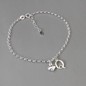 May include: A silver chain bracelet with a heart charm and a letter Q charm.