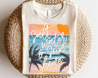 May include: A beige t-shirt with a vintage-style graphic of a sunset over the ocean with palm trees and the text "Salt Water & Sun Shine".