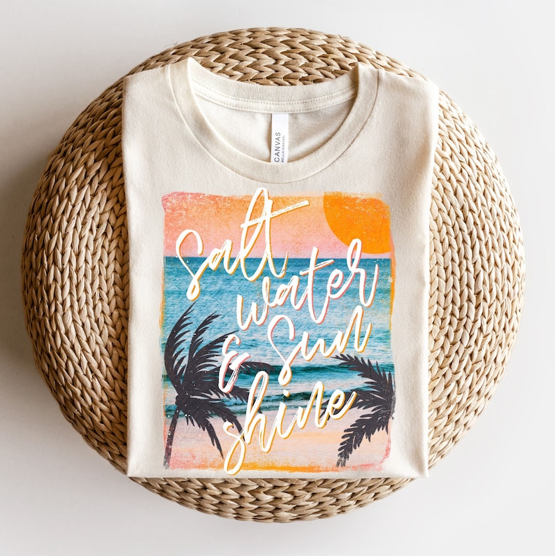 May include: A beige t-shirt with a vintage-style graphic of a sunset over the ocean with palm trees and the text "Salt Water & Sun Shine".