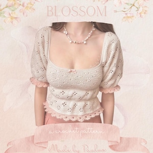 May include: Cream-colored crochet top with short, puffed sleeves and a square neckline. The top features a scalloped edge and a small pink bow. The word "BLOSSOM" is at the top, and the text "a crochet pattern Made by Paulus" is at the bottom.
