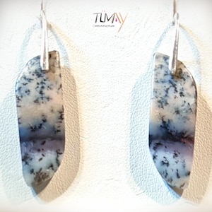 Peut inclure: Boucles d'oreilles pendantes avec une pierre naturelle aux motifs noirs, blancs et violets. Les boucles sont suspendues à des crochets argentés. La marque "TUMAY Creations" est visible en haut à droite.