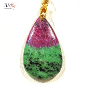 Peut inclure: Un pendentif en forme de larme avec une pierre précieuse verte et rose. La pierre précieuse est un mélange de vert et de rose, avec une couleur vert foncé en bas et une couleur rose plus claire en haut. Le pendentif est attaché à une chaîne en or.