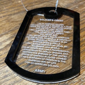 May include: A black and clear plastic dog tag with the text "SOLDIER'S CREED" and a list of the soldier's creed in white text. The bottom of the tag reads "ARMY".