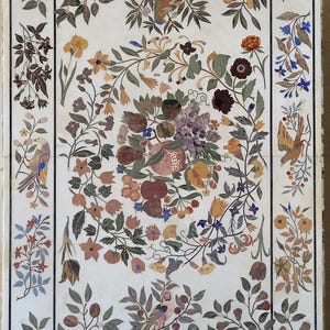 Könnte beinhalten: Ein rechteckiger Marmortisch mit einem aufwendigen Intarsienmuster. Das Design zeigt farbenfrohe Früchte, Blumen und Vögel, die von einem Rand aus Blättern und Blüten umrahmt werden. Die Farbpalette umfasst Rot, Blau, Gelb und Grün.