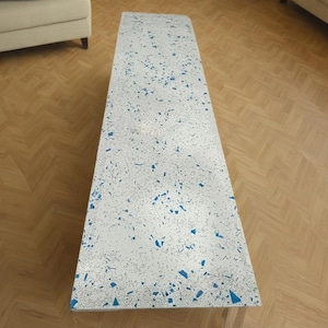 May include: A long, rectangular table with a white surface and blue flecks throughout. The table is made of a speckled material.