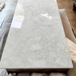 Puede incluir: Mesa de centro de mármol blanco con acabado brillante. La mesa tiene forma rectangular y un marco de madera marrón.