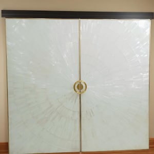 以下が含まれることがあります： 真珠貝のような素材でできた、放射状のパターンを持つ白いダブルドア。真鍮製の丸い取っ手が付いています。