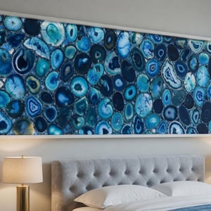 Pode incluir: Grande obra de arte de parede retangular com um mosaico de fatias de pedra de ágata azul e branca. A obra de arte é emoldurada em uma borda branca e pendurada acima de uma cama. As fatias de ágata variam em tamanho e tom, criando um padrão.