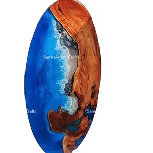 Pode incluir: Uma mesa oval de madeira com uma incrusta&ccedil;&atilde;o de resina ep&oacute;xi azul e branca que se assemelha a uma onda do oceano. A madeira &eacute; de uma cor castanho rica e a resina &eacute; de um azul vibrante com acentos brancos. A mesa tem um di&acirc;metro aproximado de 45 cm.