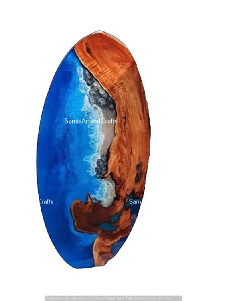 Pode incluir: Uma mesa oval de madeira com uma incrusta&ccedil;&atilde;o de resina ep&oacute;xi azul e branca que se assemelha a uma onda do oceano. A madeira &eacute; de uma cor castanho rica e a resina &eacute; de um azul vibrante com acentos brancos. A mesa tem um di&acirc;metro aproximado de 45 cm.