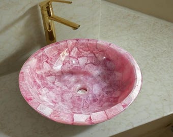 Pode incluir: Uma pia de banheiro de cerâmica rosa e branca com um design único de mosaico. A pia é redonda e tem um acabamento liso e polido.