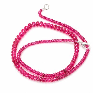 May include: A necklace composed of small, translucent, deep pink, round beads strung together. The strand features a silver-toned metal lobster claw clasp at one end and a small circular ring at the other, creating a continuous circular loop.