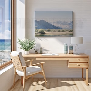May include: A light wood desk with a matching chair, a landscape painting, and a window with a view of the ocean. The desk has a lamp, two decorative bottles, and a potted plant. The chair has a white cushion.