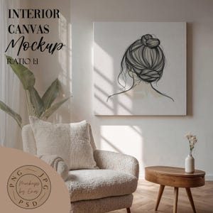 May include: A white armchair with a cream-colored throw pillow sits in a room with a white wall. A square canvas print of a black and white line drawing of a woman's back with her hair in a bun hangs on the wall. A small wooden table with a vase of white flowers sits in the foreground.