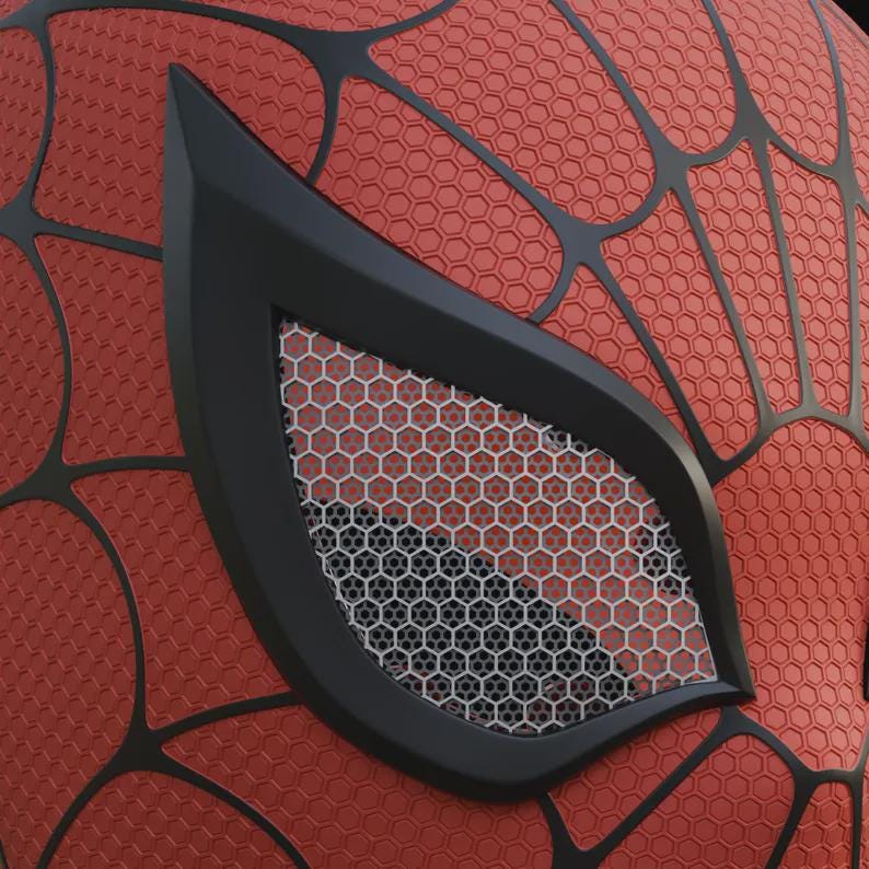 May include: Close-up of a red and black Spider-Man mask. The mask features a textured red surface with a black web pattern. The eye is outlined in black with a white and gray honeycomb mesh.