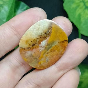 May include: A close-up of a yellow, orange, and white agate cabochon. The stone has a swirling pattern and is smooth and polished.